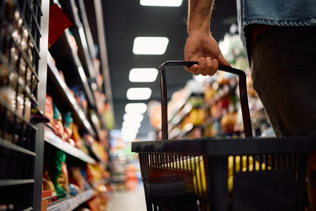 Person holding a shopping basket in a food aisle of a supermarket